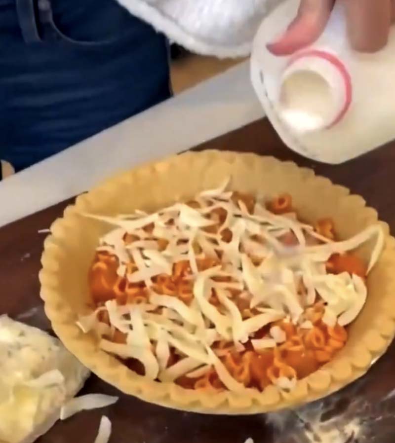 woman pouring milk inot a pie filled with spaghetti-o