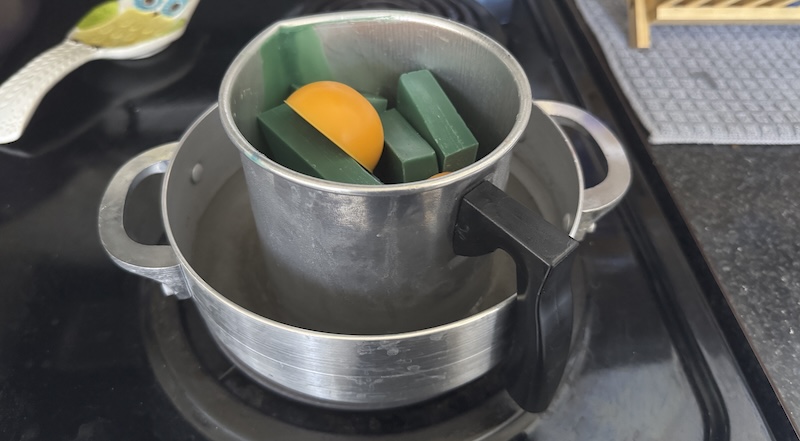 photo of my double boiler setup on the stove with green and yellow wax blocks starting to melt
