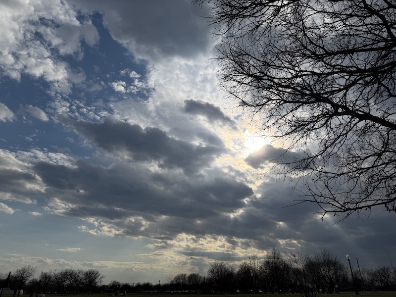 photo of the sky at the park. the sky is huge and the clouds are plentiful, and the sun is peeking out a little bit from behind them. it's quite majestic looking