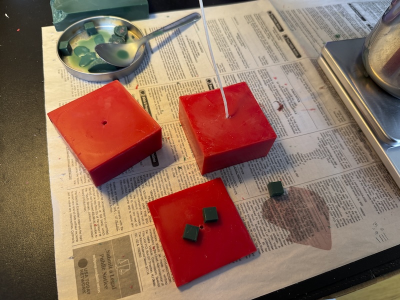 photo of some red rectangular prism candles and little green cubes, scattered on newspaper as i'm testing and assembling them