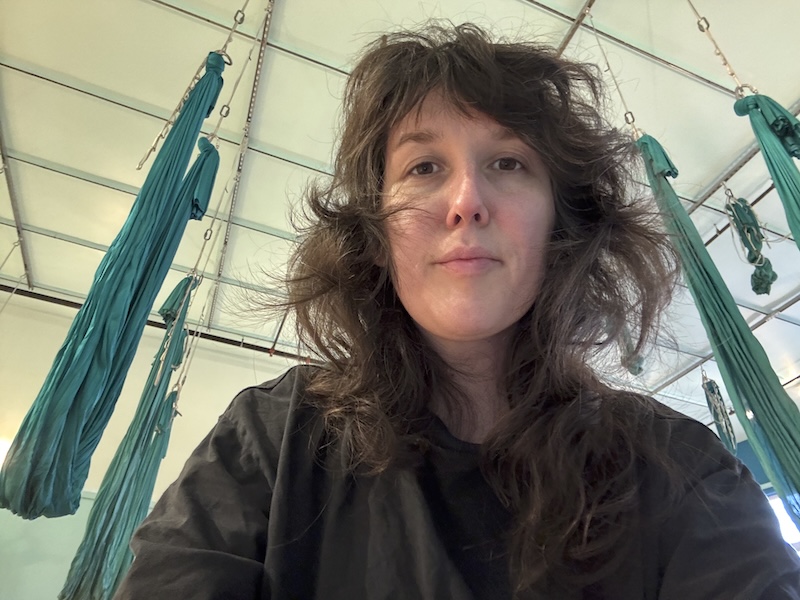 selfie of me in the aerial yoga studio, behind me you can see a bunch of turquoise colored silks hanging from rigging points across the ceiling