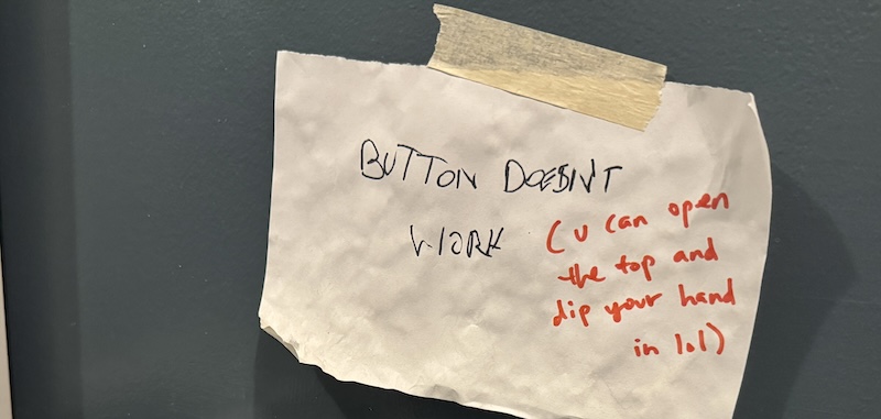 photo of the bathroom sign saying "button doesn't work (u can open the top and dip your hand in lol)"