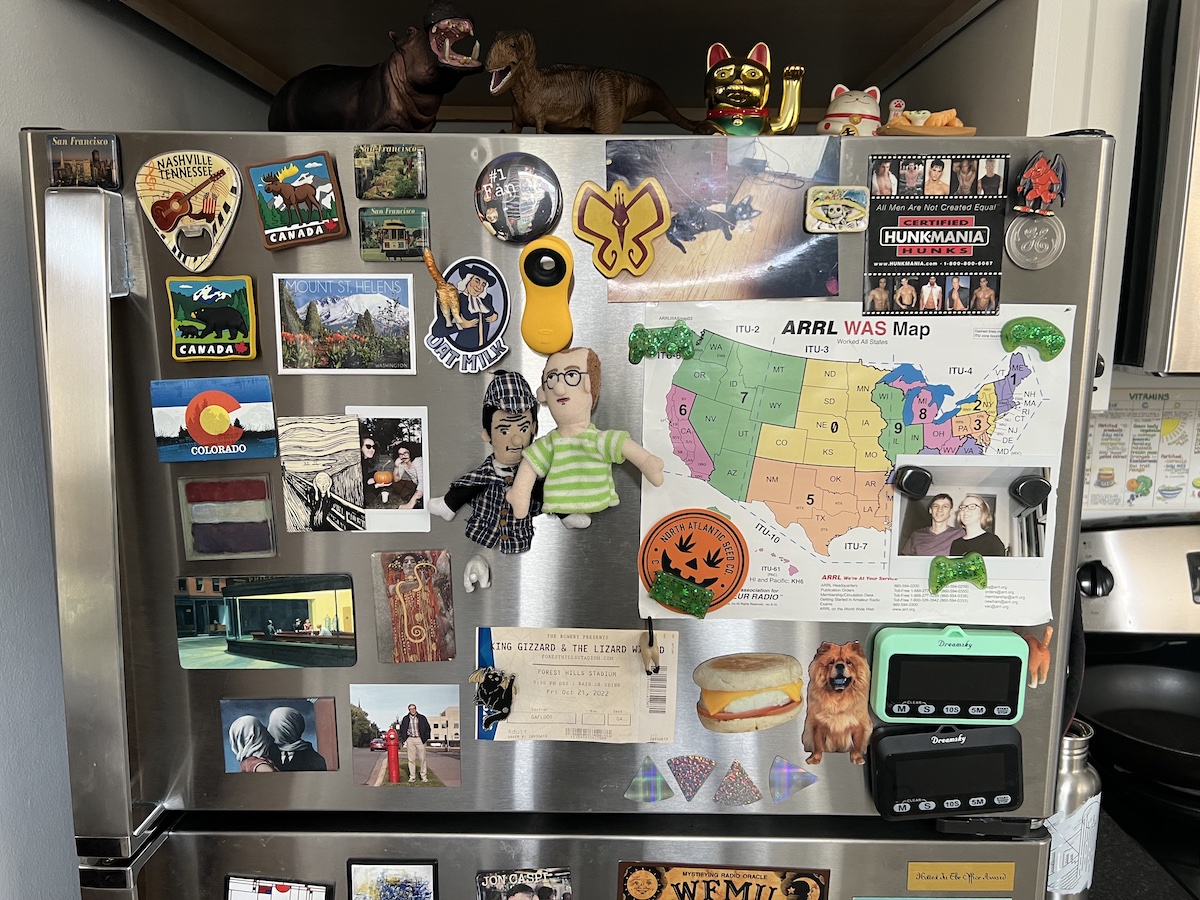 a steel fridge freezer door filled entirely with magnets, gizmos and photos of friends
