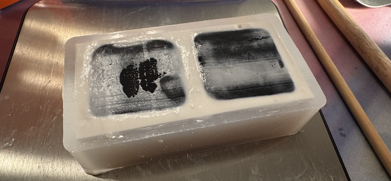 a rectangle silicone mold filled with white moldgel holding two black polymer clay butter tabs