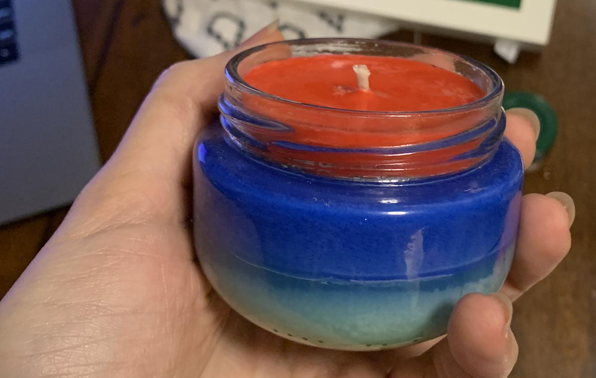 photo of my hand holding a small, complete candle with turquoise, cobalt blue and red layers