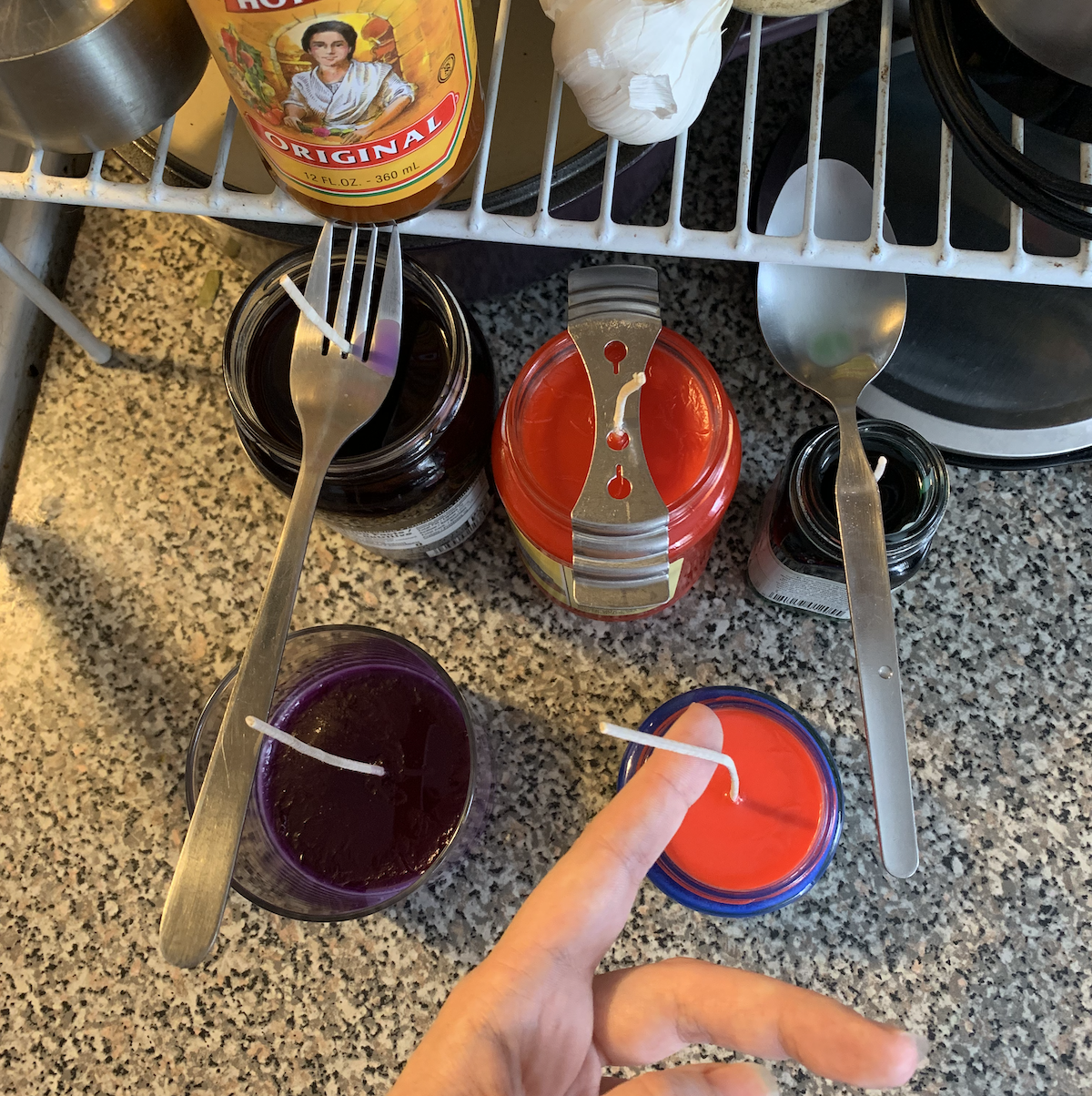 photo of 4 candles set to harden, one wick is held by a fork held by a bottle of cholula hot sauce