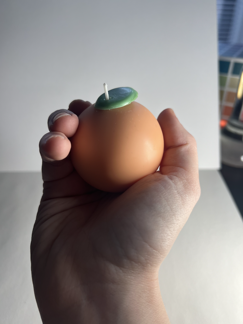 photo of my handle holding up a little, perfect orange fruit candle