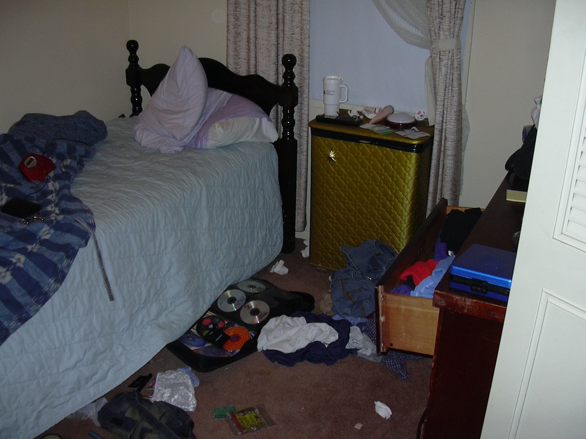 photo of a very messy, small room. drawers are open, bed is unmade, gigantic cd wallet is open on the floor with clothes and a road flare. on my bed is a portable cd player