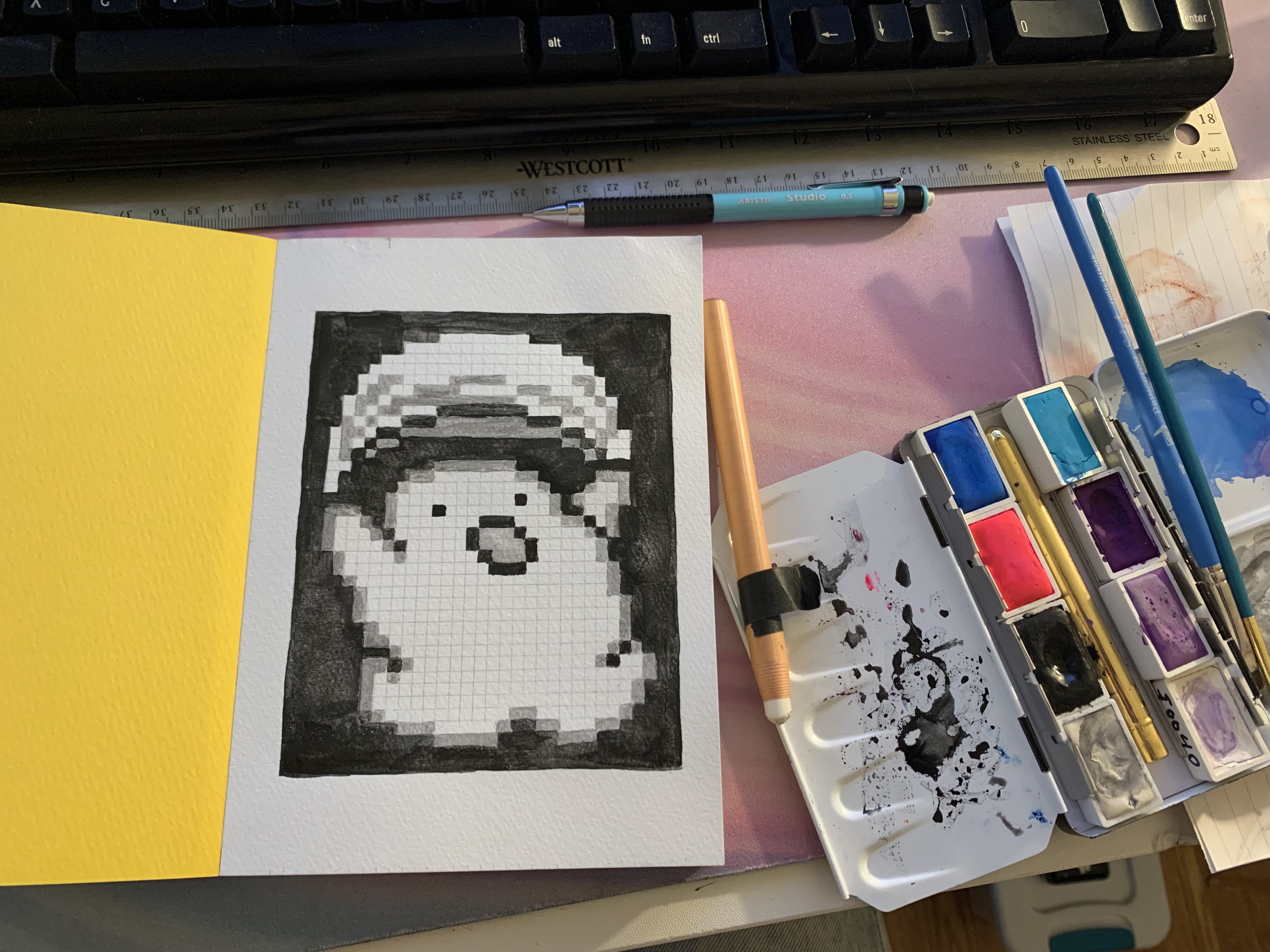 photograph of the pixel painting of noobow next to my watercolors and tools