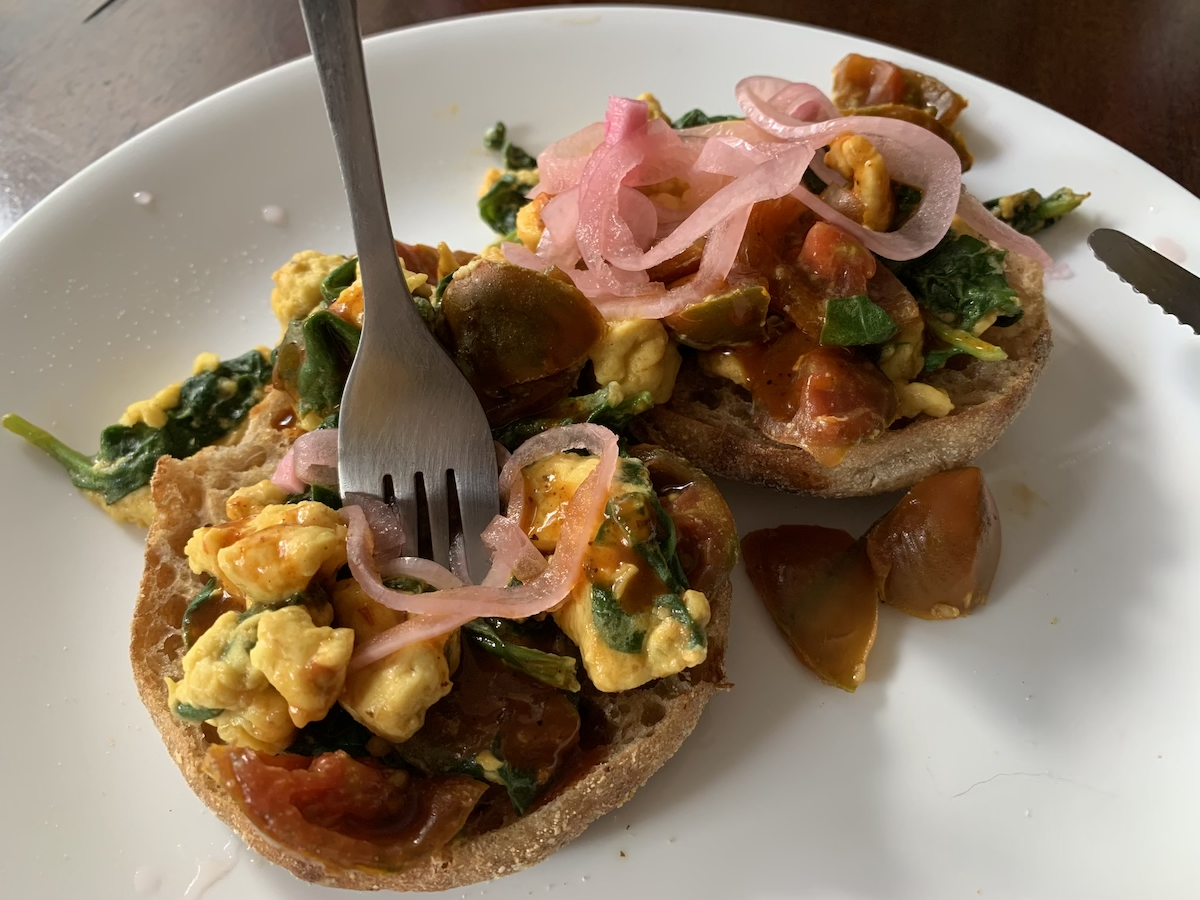 a photo of a plate with english muffins and vegan eggs, tomatoes, spinach and pickled red onions on top