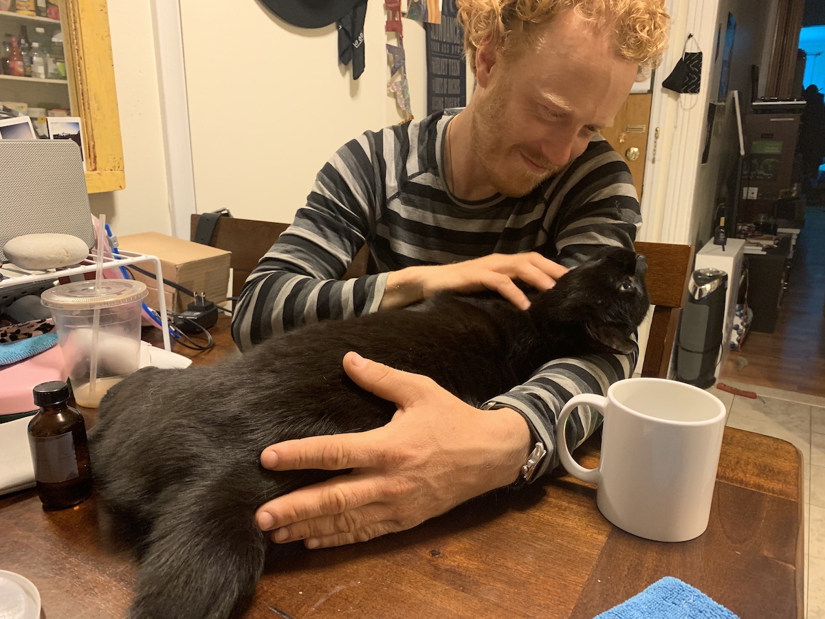 photograph of pumagreg sprawled out on the table near tyler who is petting him